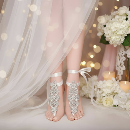 A close-up of a woman's foot wearing a white barefoot sandal with rhinestone embellishments and a lace-up design.